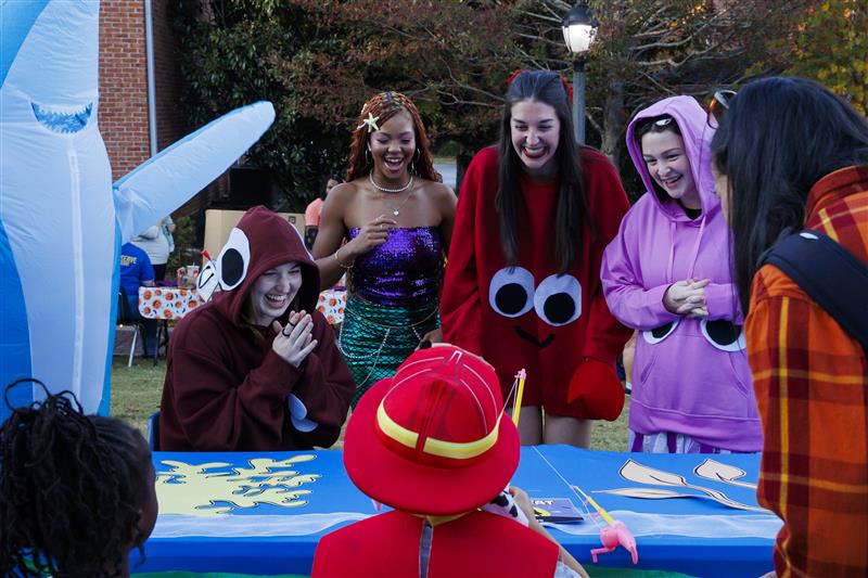 沙巴官网 Students standing behind a table wearing fun halloween costumes and handing out candy to children trick-or-treating.