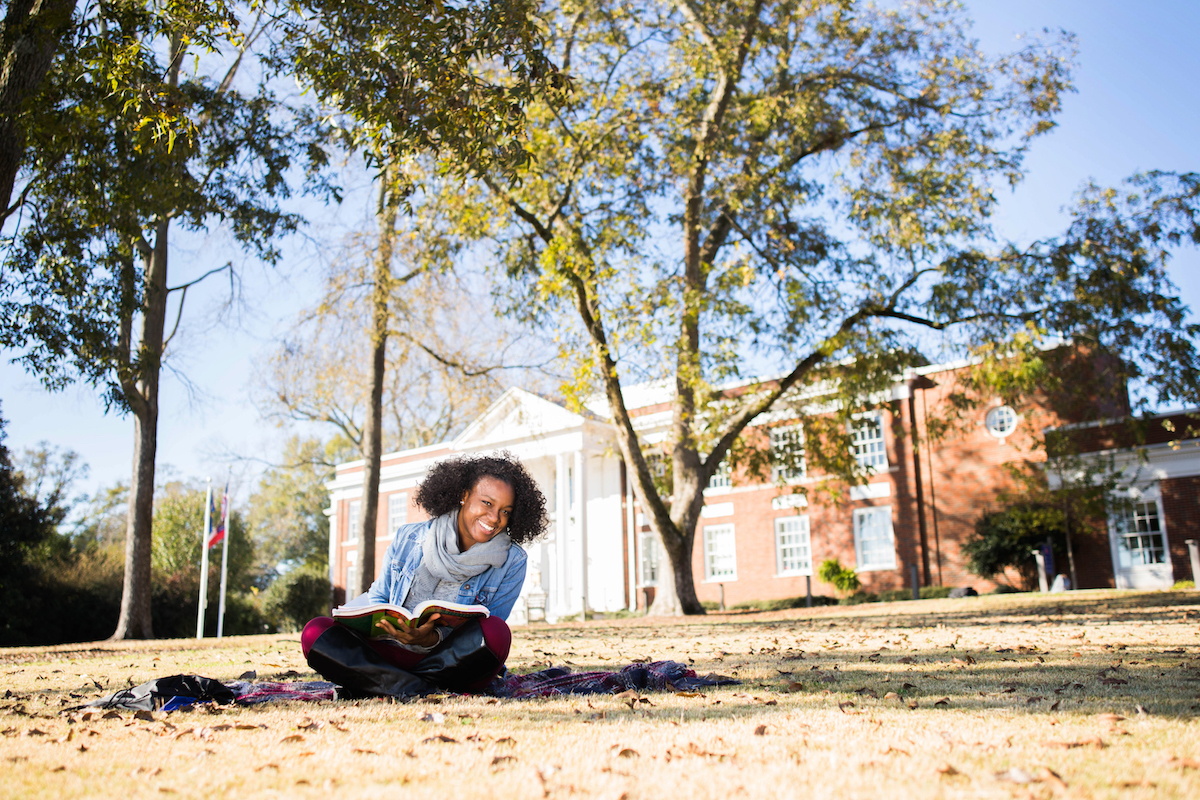 Student smiling and studying in the grass.