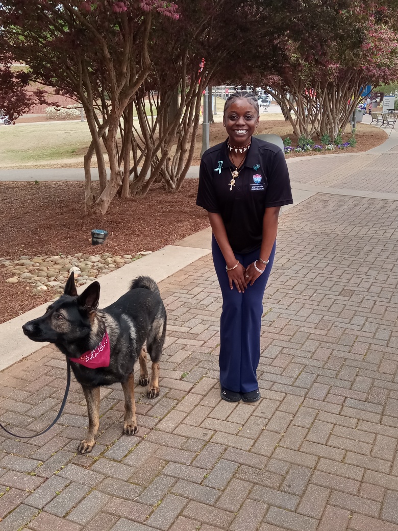 Female student smiling standing in the pedestrian next to a dog wearing a red bandana.