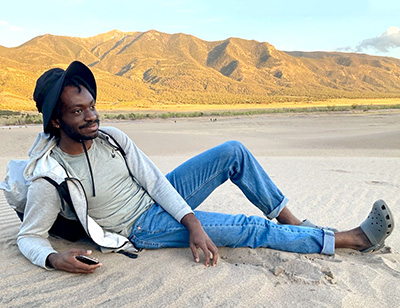 student lying in sand with mountains in back