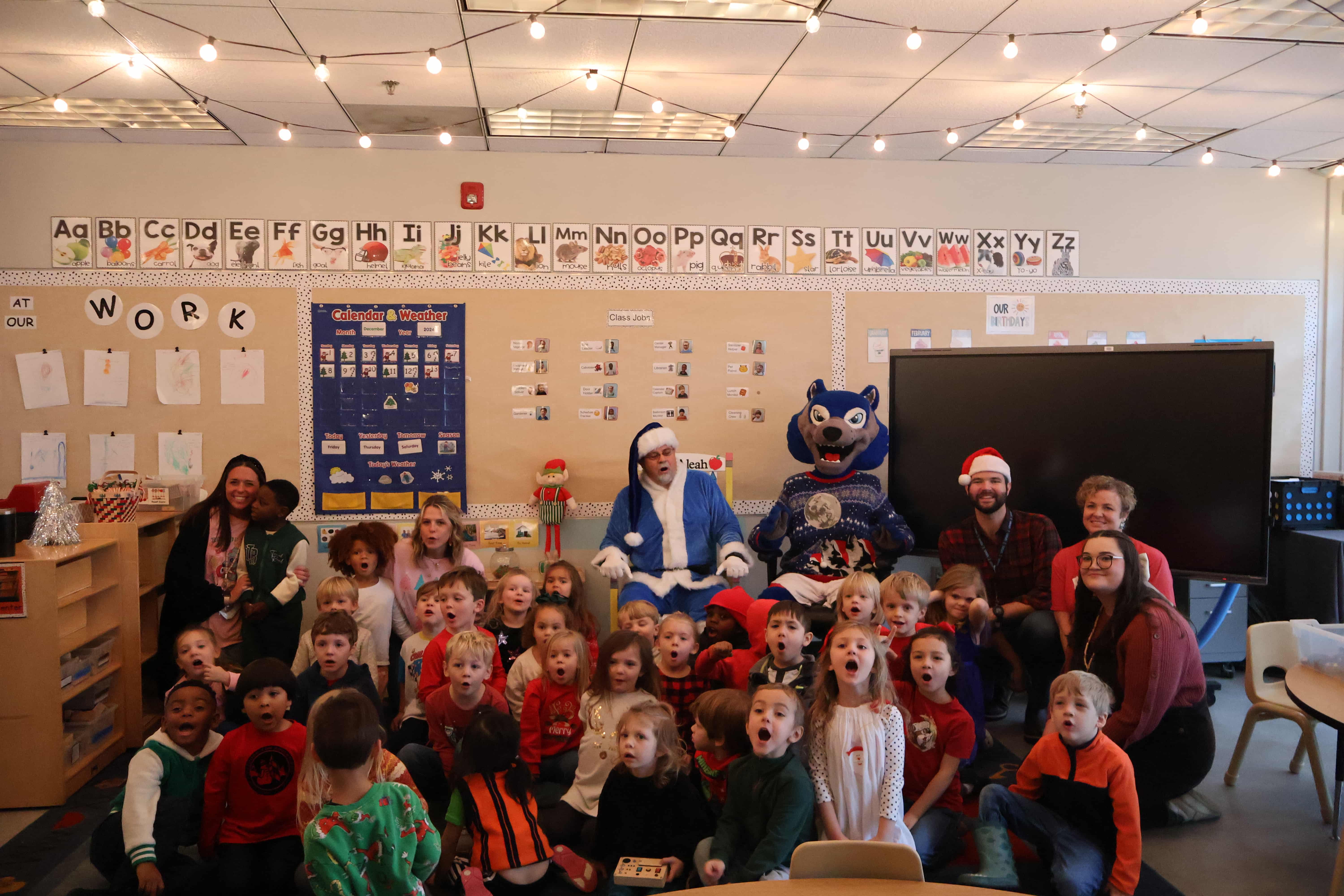 Pre-K students with the College of Education Dean dressed in a 沙巴官网 blue santa suit. They are saying "ho ho ho" to the camera.