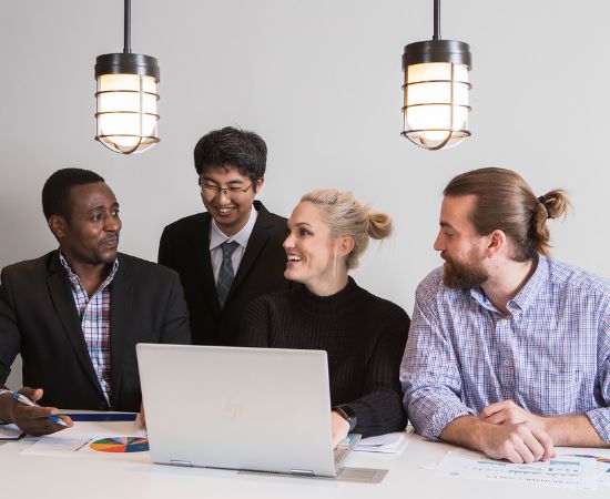 Four students in business attire working on a laptop