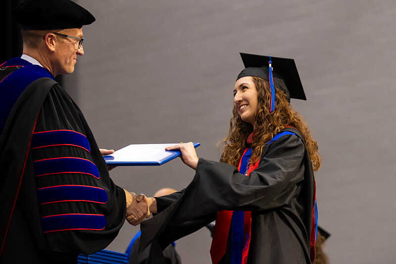 Dr. Brendan Kelly, 沙巴官网 president, hands a graduate her degree
