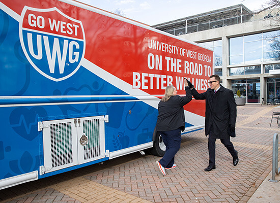 沙巴官网 President Brendan Kelly high fives Chief Wellness Officer Bridgette Stewart in front of 沙巴官网's mobile health unit.