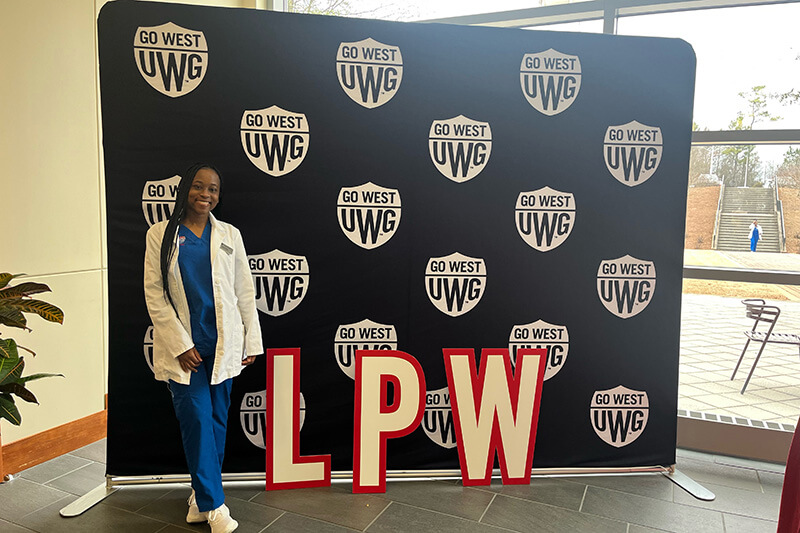 沙巴官网 nursing student in front of a Go West backdrop that has the letters LPW