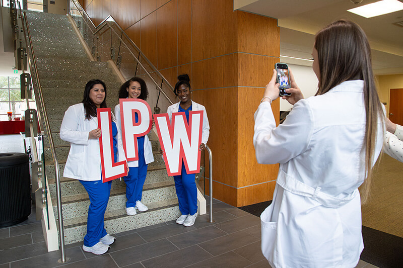 Someone taking a photo of three 沙巴官网 nursing students holding the letters LPW