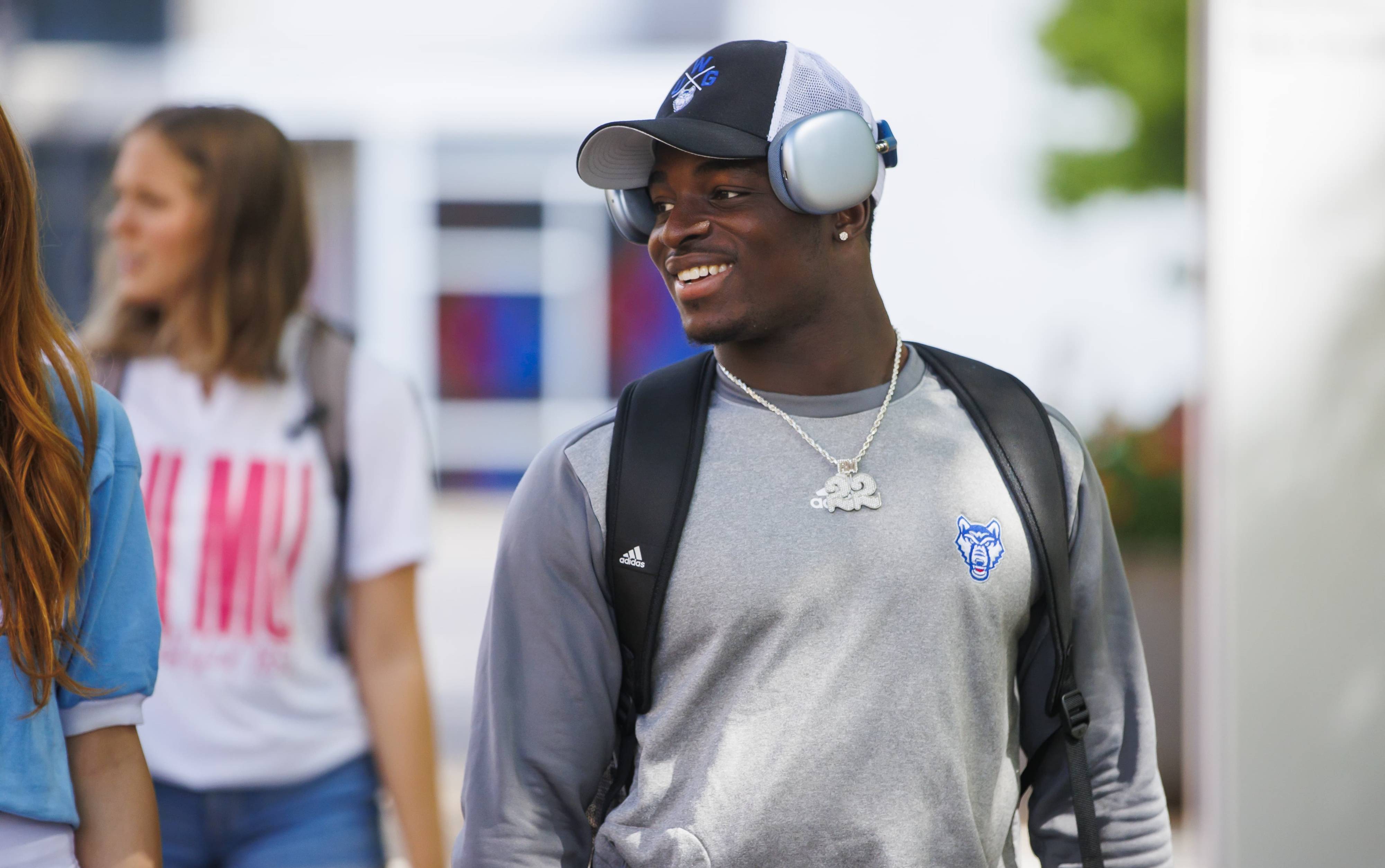 An African-American male student walking on campus smiling and wearing a 沙巴官网 hat and long sleeve shirt.