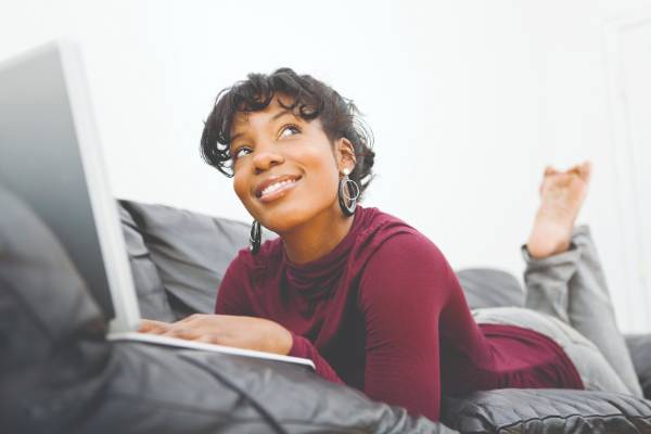 Woman laying on couch and smiling with laptop